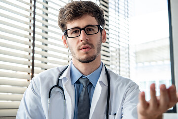 Young male doctor looking at camera explaining and talking with patient online via video calling, distance medical consulting service and telehealth concepts