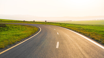Asphalt road between green farm fields with blue sky and clouds