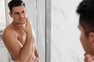 Fototapeta na wymiar Handsome man touching his smooth face after shaving near mirror in bathroom