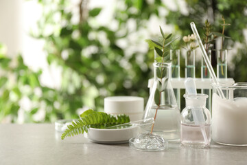 Natural ingredients for cosmetic products and laboratory glassware on grey table against blurred...