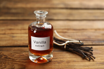 Aromatic vanilla extract and dry pods on wooden table, space for text