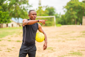 candid image of african guy. holding a football and pointing one finger- outdoor soccer concept