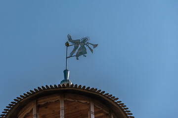 Fototapeta na wymiar Weather vane in the form of a trumpeting angel on the dome of the tower of an ancient fortress against the sky.