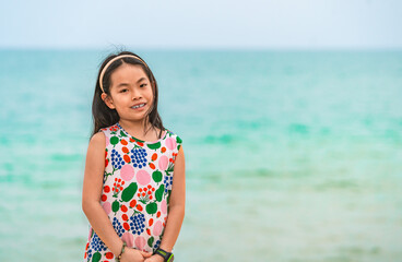 Portrait Asian little child girl on a beach, background of blurred sea and sky. Child girl with long black hair, smile, eyes looking at camera, blank space for copy and design.