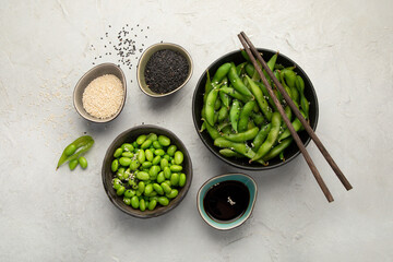 Raw edamame soya beans with salt and sauce on light gray background.