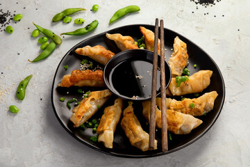 Fried gyoza dumplings with soy sauce and onion on light gray background.
