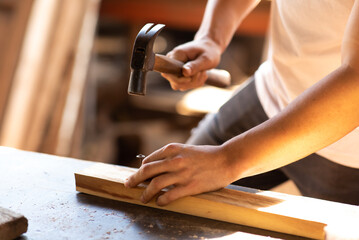 Close up of carpenter hammering a nail into wooden board. Construction industry concept.