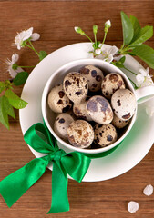 Easter background. Quail eggs in a white cup and a branch of blooming cherry on a wooden table