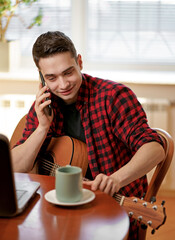 A young man learns to play the guitar using the Internet, laptop, online lesson. Hobby and leisure concept