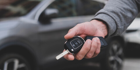 Man in front of the new car and holding keys. Salesman is carrying the car keys delivered to the...