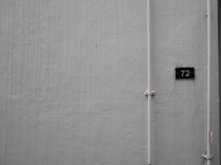 small metal 72 plate mounted on white painted wall with narrow white pipe