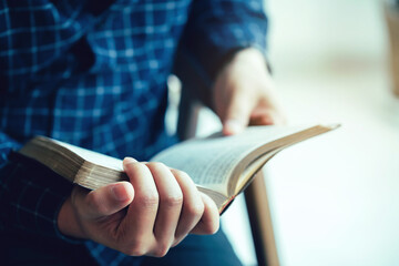 man sitting while reading bible or book over concrete wall with window light