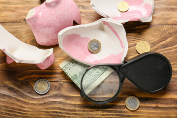 Broken piggy bank with money and magnifier on wooden background. Concept of bankruptcy