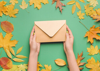 Female hands with envelope and autumn leaves on color background