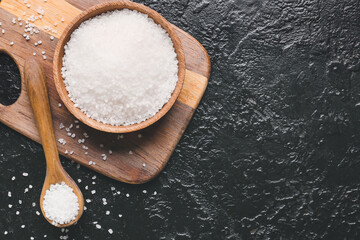 Bowl and spoon with salt on dark background