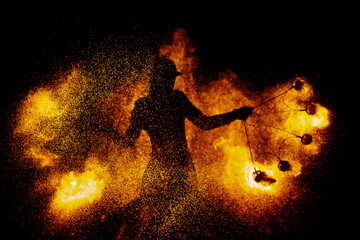 Silhouette of a female magician doing a fire show. Fire sparks fly around a woman. The magician is wearing a leather cloak and hat.