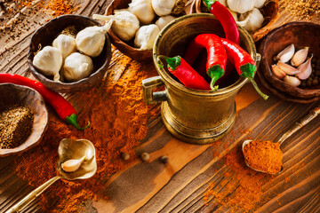 Pods red Chilean pepper in old brass mortar. Phials with garlic and pepper powder. Brass spoon shaped leaves with slices of garlic and pepper powder. Ingredients for cooking on an old wooden surface.