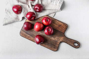 Board with fresh red apples on light background
