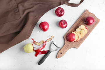 Board with cut red apples and peeler on table