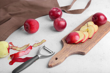Board with cut red apples and peeler on table