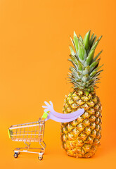 Funny pineapple with shopping cart on color background