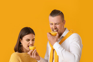 Stylish young couple with lemon on yellow background
