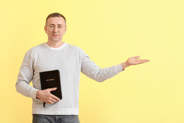 Man with Bible showing something on color background