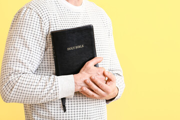 Man with Bible on color background, closeup