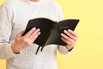 Man with Bible on color background, closeup