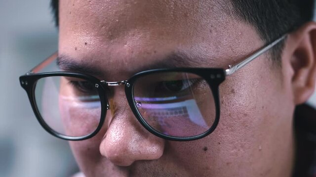 Close up moving eye and face of Asian man hacker IT using computer hack password security of online network. Reflection on glasses show detail this guy typing code on keyboard of notebook