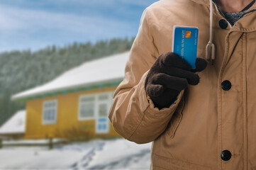 Man with credit card on the background of winter cottage, concept of house and real estate deal