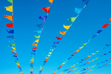 Triangular flags of different colours develop in the wind against the blue clear sky.