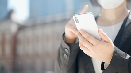 屋外でスマートフォンを操作するマスク姿のビジネスウーマン
