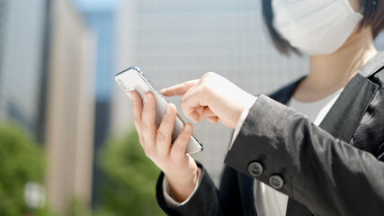 屋外でスマートフォンを操作するマスク姿のビジネスウーマン