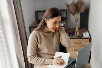 Young beautiful woman working in the home uses a laptop and mobile phone. Female writing in block note