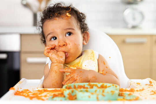 Cute messy baby sucking thumb in high chair
