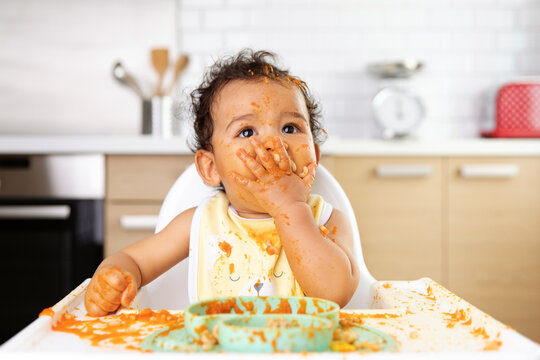 Cute baby in high chair eating messily with hands