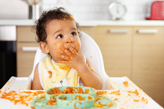 Funny baby in high chair with guilty messy face