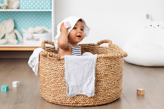 Cute baby sitting in laundry basket with clothes on head