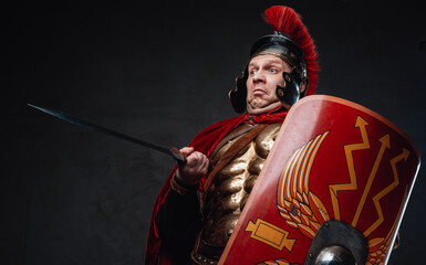 Clumsy roman soldier points his sword against dark background
