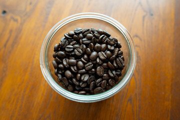 木のテーブルの上に置いた瓶に入ってるコーヒー豆