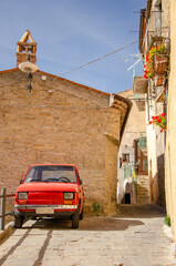 Typical street in Italy with a parked small red Fiat 500 car.