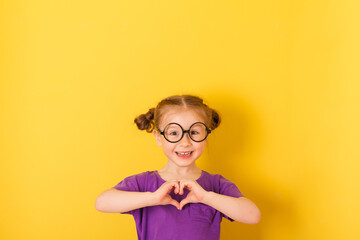 Little cute caucasian funny happy smile kid child baby girl with glasses glasses in purple T-shirt on yellow wall background. children studio portrait about love.