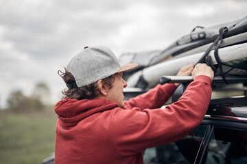 Windsurfer and camper packing and unpacking from a car's roof rack in nature.