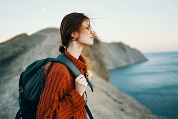 woman tourist with a backpack in a sweater are resting in the mountains near the sea and looking at the sky