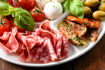 Piatto con fette di salame, pomodori secchi, mozzarella e olive, antipasto italiano  