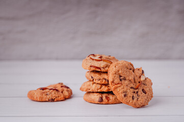 Piles of delicious chocolate chip cookies on a white plate with a milk bottle. Pastry utensils with white linen napkins on a wooden table. Delicious on a white plate with a bottle of milk.