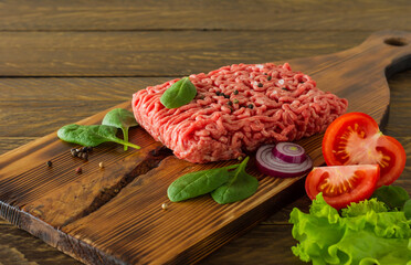 Raw minced beef meat on a wooden cutting board with vegetables and spices. Cooking and healthy eating concept.