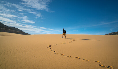 Traveler cum hiker walking in the desert leaving trail of footprints. 