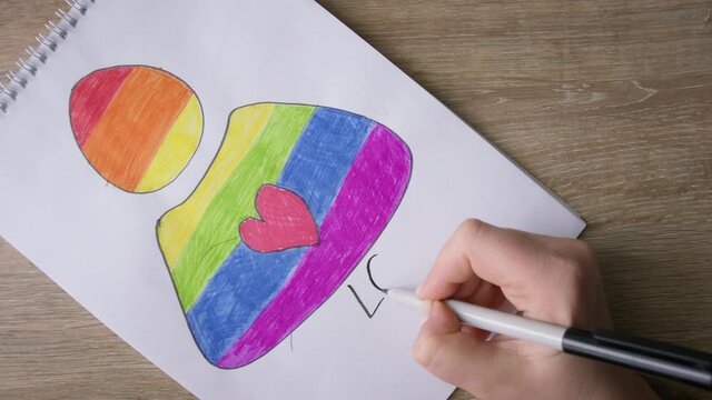 Female hands write LOVE IS FOR ALL on figure of rainbow colors girl.